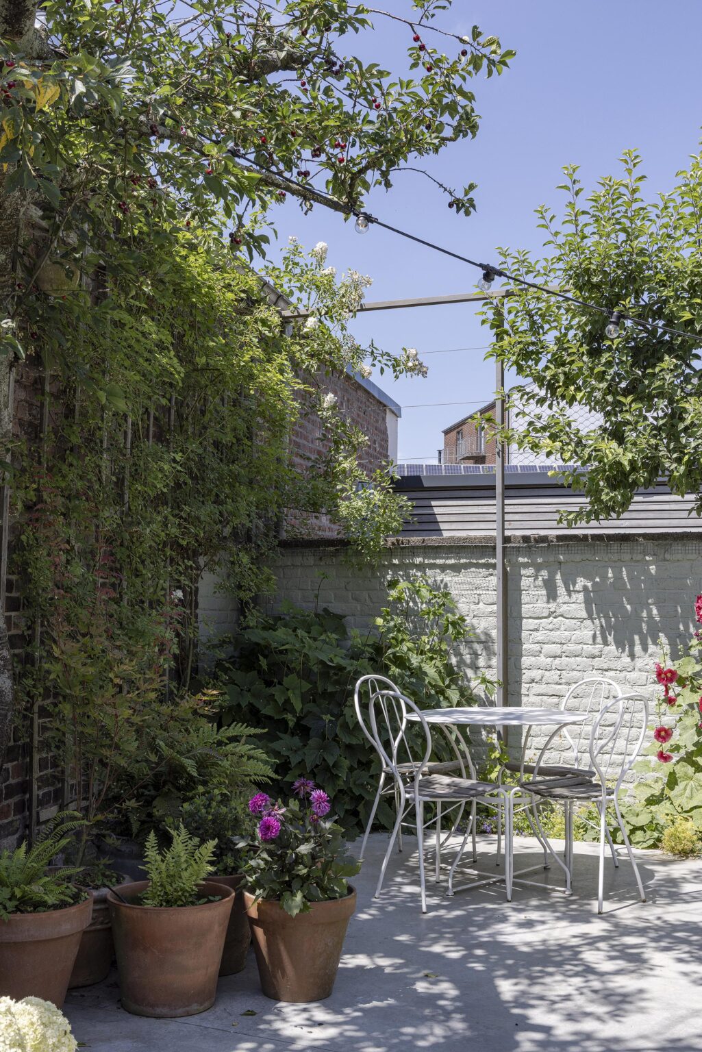 Petite terrasse avec table ronde blanche et pots de fleurs.