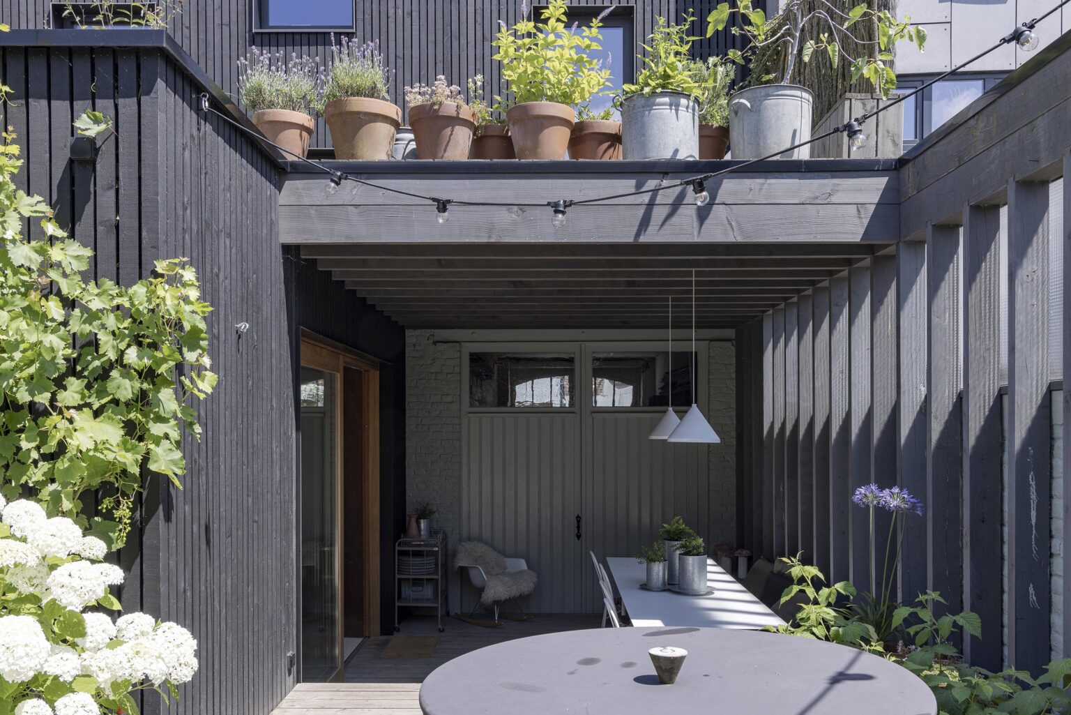 Terrasse couverte avec table à manger et pots de fleurs sur la toiture.